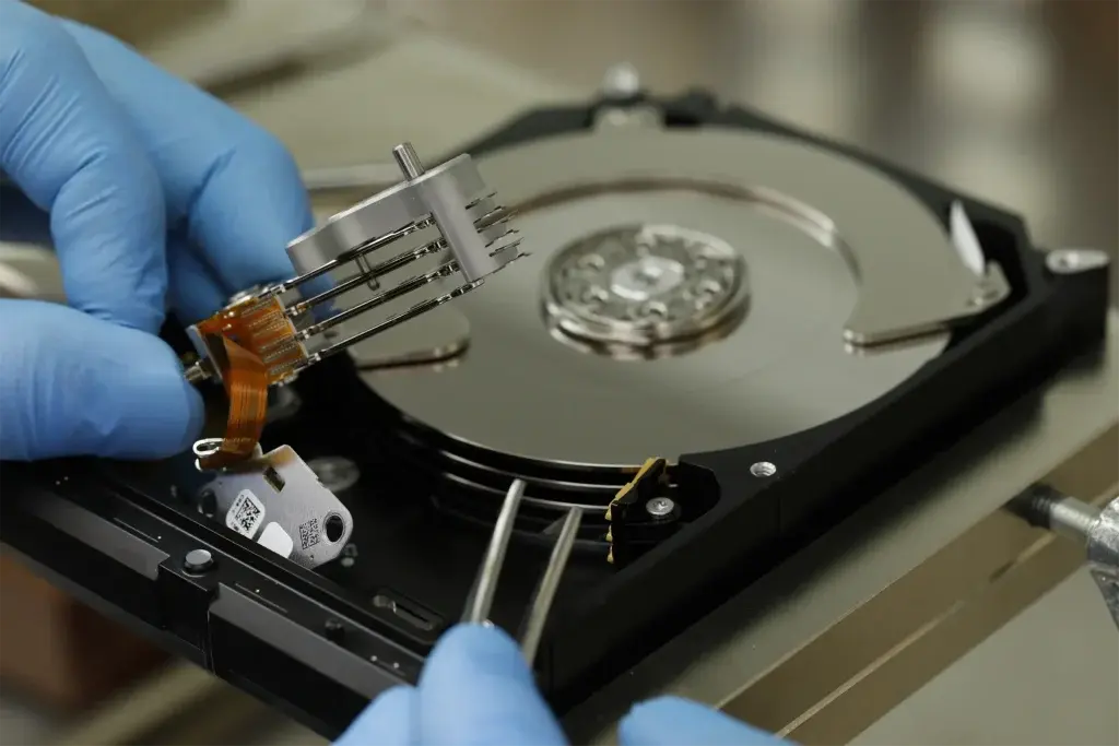 Technician handling an open hard drive’s read/write head assembly.