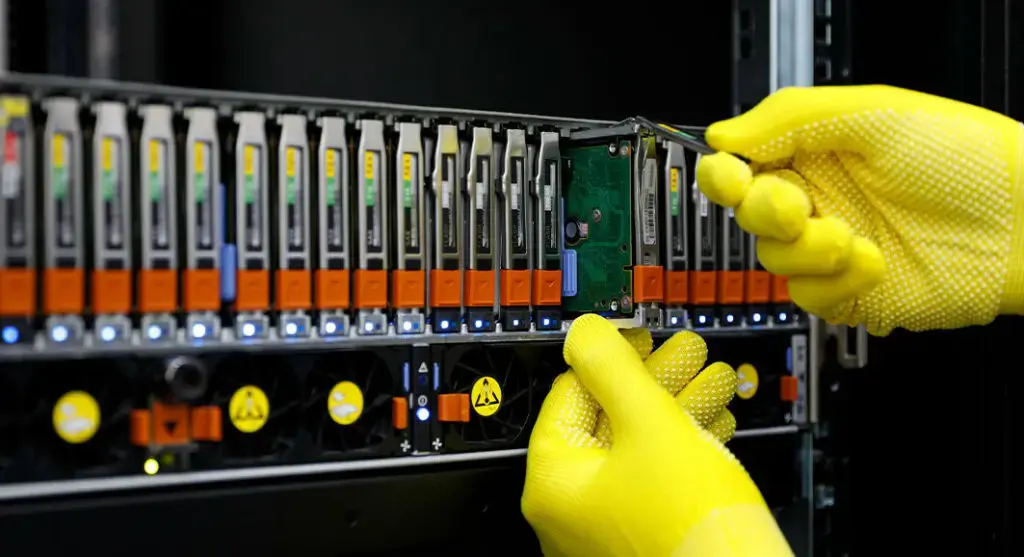 Technician in yellow gloves replacing a hard drive in a server rack.